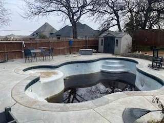 Partially demolished inground swimming pool in North Richland Hills TX backyard, concrete shell drained and stripped, deck intact