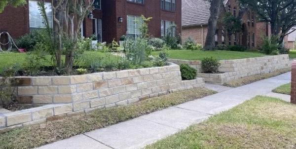 Granbury stone retaining wall with raised planting bed along residential front yard sidewalk in Colleyville TX