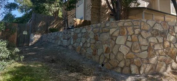 Natural stone retaining wall with irregular cut stones supporting a sloped residential yard beside a brick home in Lewisville, TX