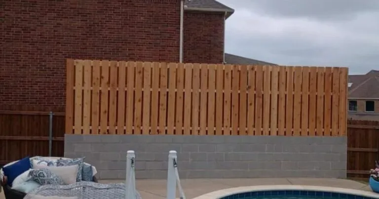 New concrete block retaining wall topped with fresh cedar privacy fence beside a backyard pool in Fort Worth, TX