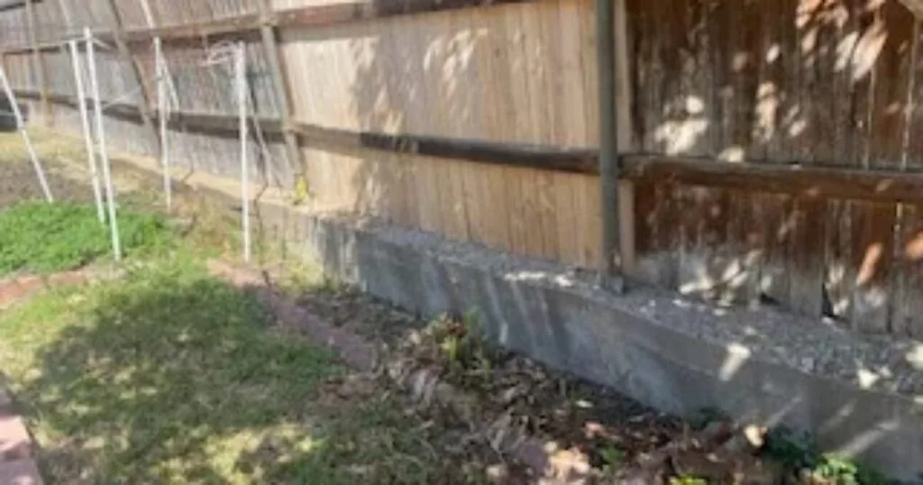 Aging concrete block retaining wall along wood privacy fence in Dallas backyard, candidate for Milsap stone replacement
