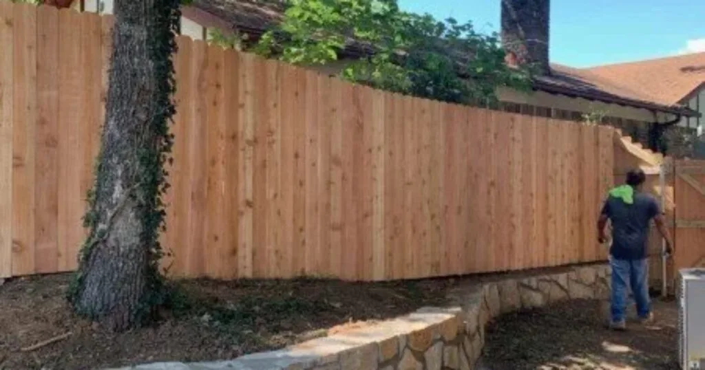 New natural stone retaining wall replacing a failed crosstie wall along a wood privacy fence in a Carrollton, TX backyard