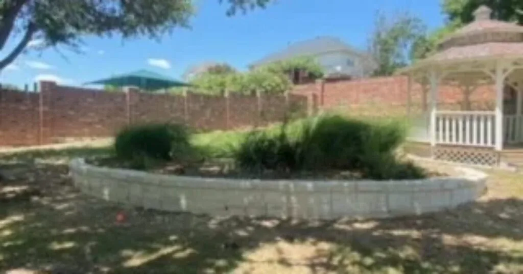 Curved concrete block garden retaining wall replacing old cross-tie wall, with ornamental shrubs and white gazebo in Carrollton TX backyard