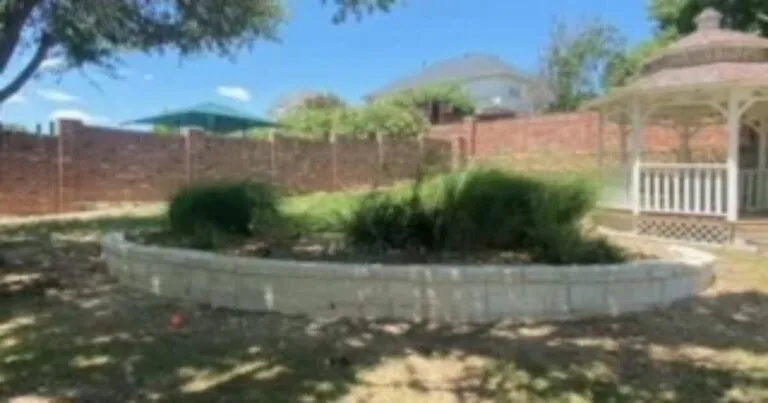 Curved concrete block garden retaining wall replacing old cross-tie wall, with ornamental shrubs and white gazebo in Carrollton TX backyard