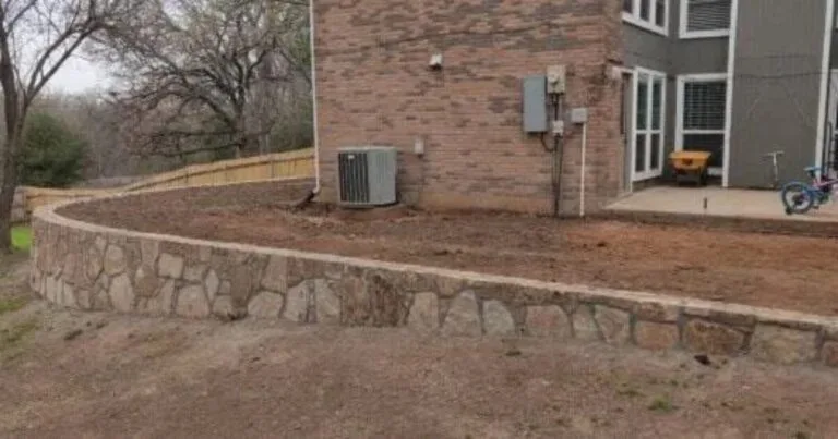 Curved natural stone retaining wall along brick home's backyard in Euless TX, holding graded soil to protect foundation