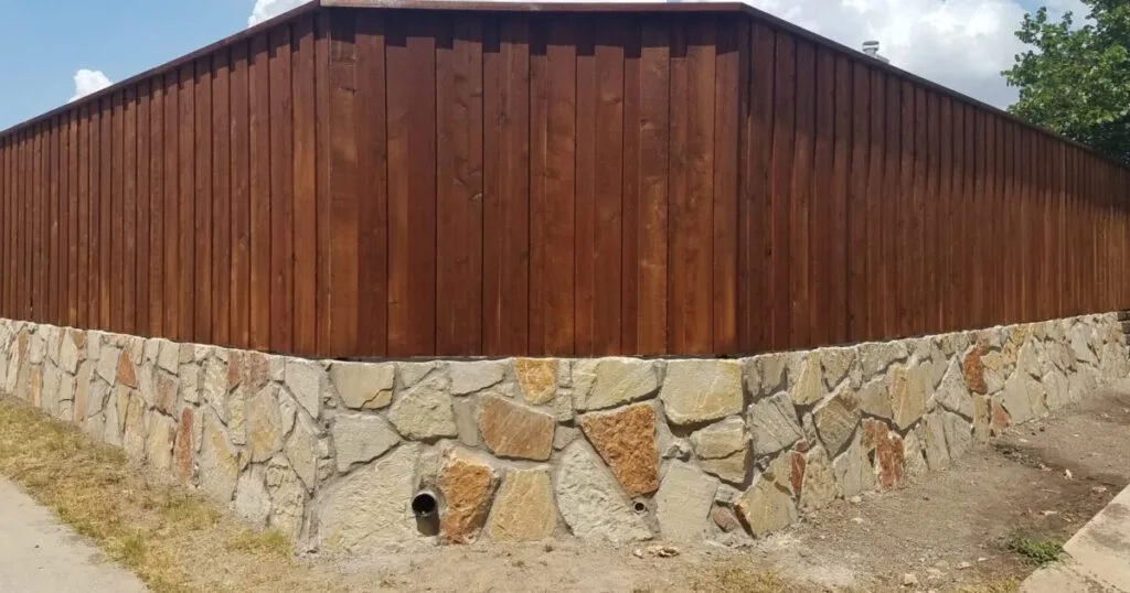Granbury stone retaining wall with drainage pipes supporting a cedar privacy fence along a DFW residential property boundary