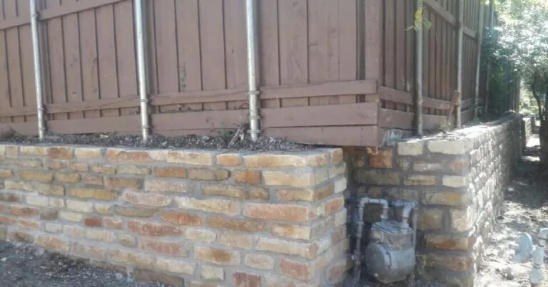 Newly built Granbury stone retaining wall supporting a wood fence along a Dallas residential property, with visible gas meter at corner