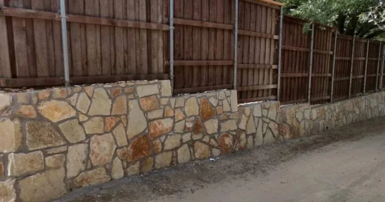 New Granbury stone retaining wall supporting a wood privacy fence along a residential property in Dallas, TX