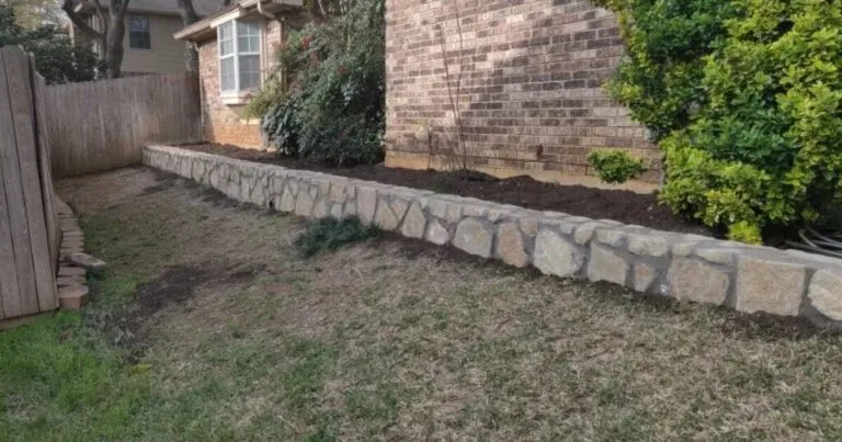 New Granbury stone retaining wall along brick home foundation creating raised planting bed in Bedford TX backyard