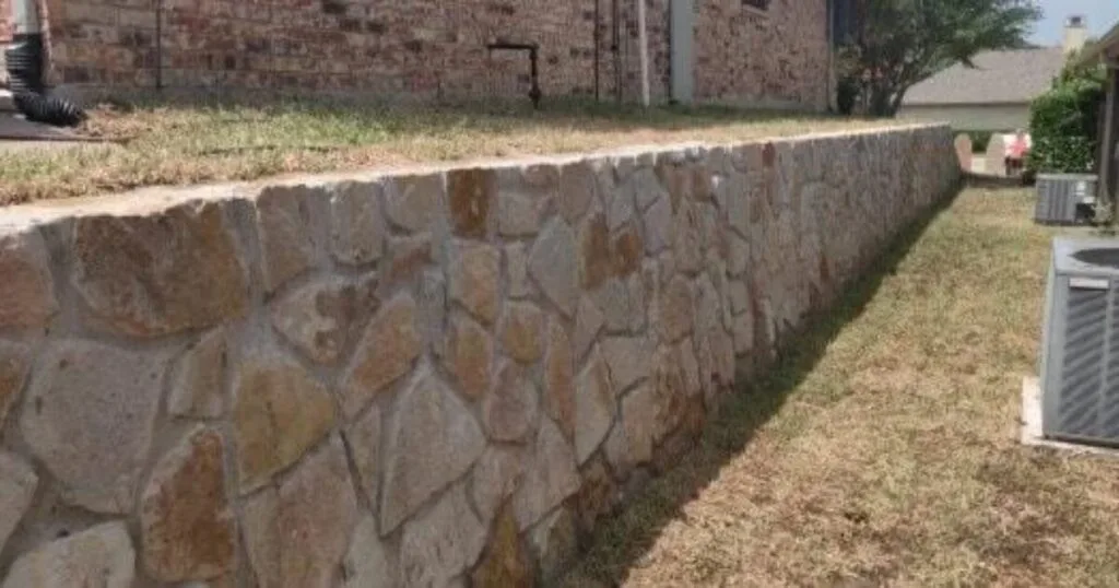 Completed Granbury stone retaining wall replacing a failed crosstie wall along a residential backyard in Carrollton, TX