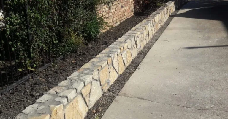 Newly built Granbury stone retaining wall along a concrete driveway, replacing an old wall beside a brick home in DFW