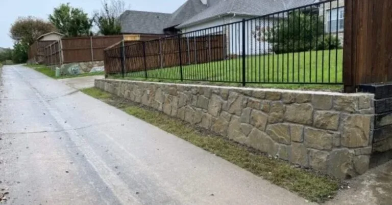 Granbury stone retaining wall along residential alley in McKinney TX, supporting raised yard behind wrought-iron and wood fence