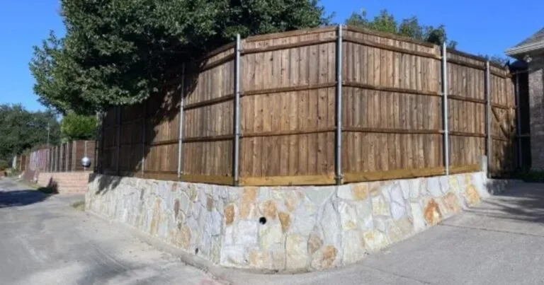 Milsap stone retaining wall base supporting a wood privacy fence at a residential corner lot in Carrollton, TX — replacing a failing cross-tie wall
