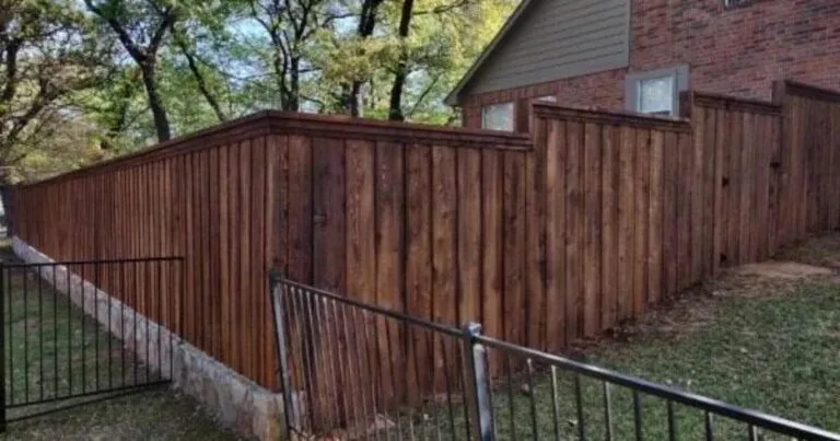 Stained cedar board-on-board privacy fence atop a Milsap stone retaining wall base beside a brick home in Carrollton, TX