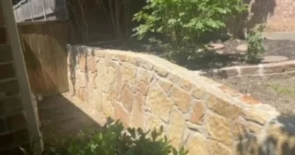 Curved natural Milsap stone retaining wall replacing an old cross-tie wall in a residential DFW backyard