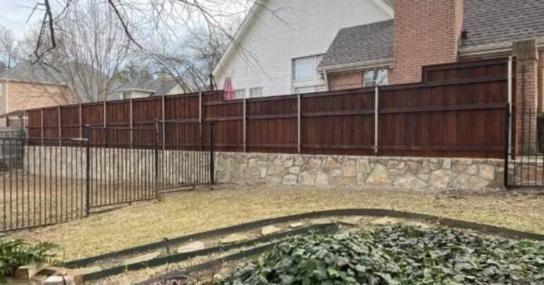 Low Milsap stone retaining wall base supporting a wood privacy fence with wrought-iron gate in a DFW residential backyard, replacing an old crosstie wall in Irving, TX.
