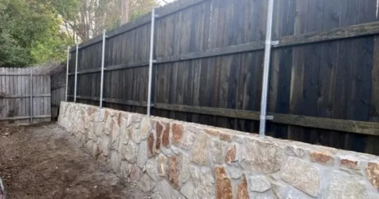 Milsap stone retaining wall replacing a failed crosstie wall along a wooden privacy fence in a Carrollton, TX backyard