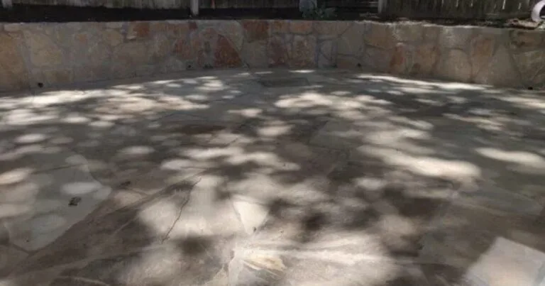 Drained empty pool interior showing flagstone patio floor and Milsap stone retaining walls on three sides, Carrollton TX backyard