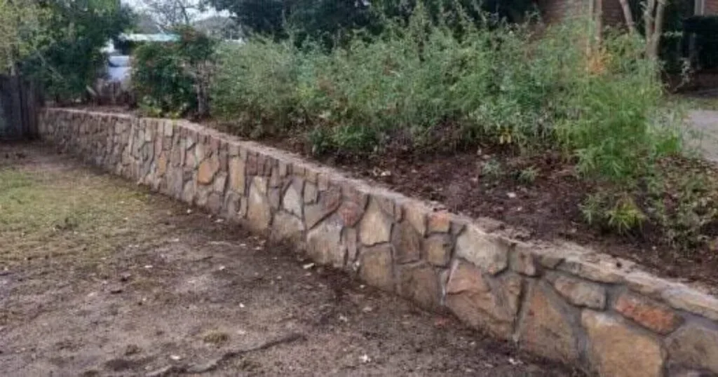 Milsap stone retaining wall replacing old cross tie wall, retaining raised planting bed with shrubs in Flower Mound, TX