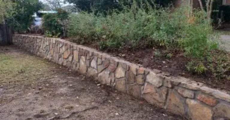 Milsap stone retaining wall replacing old cross tie wall, retaining raised planting bed with shrubs in Flower Mound, TX