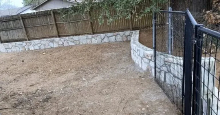 Newly built curved Milsap stone retaining wall in a Grapevine TX backyard, with graded soil and black metal gate