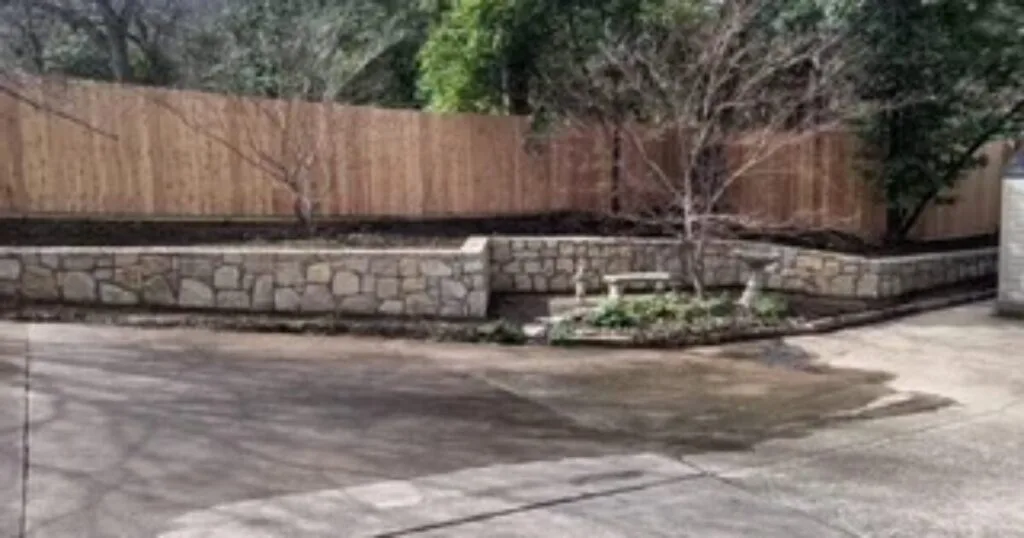 Completed Milsap stone retaining wall replacing old railroad tie wall, with raised planting bed and wood privacy fence in DFW backyard