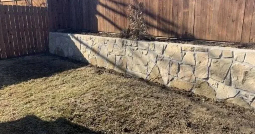 Newly built Milsap stone retaining wall replacing a deteriorated crosstie wall in a Carrollton TX backyard, with raised planting bed and wood fence
