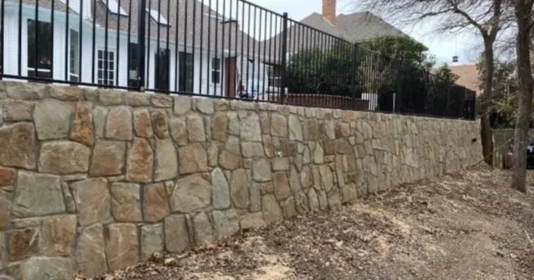Newly built Milsap stone retaining wall with black iron fence on top, supporting a residential yard in Colleyville, TX