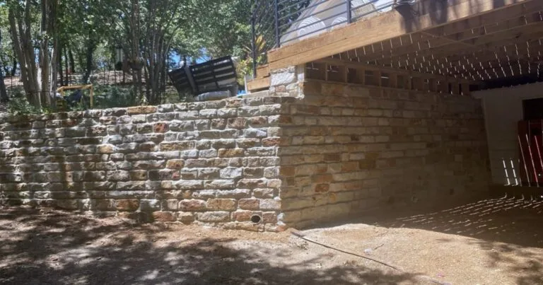 Chopped Milsap stone retaining wall replacement under a deck, built where a cross-tie and cinder block wall once stood, DFW backyard