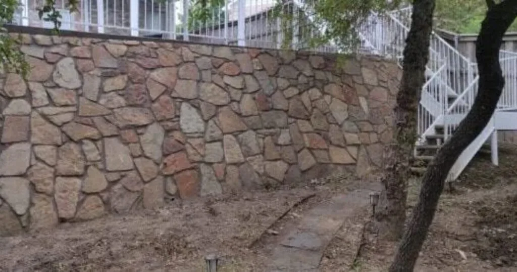 Large Milsap stone retaining wall with irregular flagstone pattern supporting elevated deck and staircase in Dallas-Fort Worth backyard