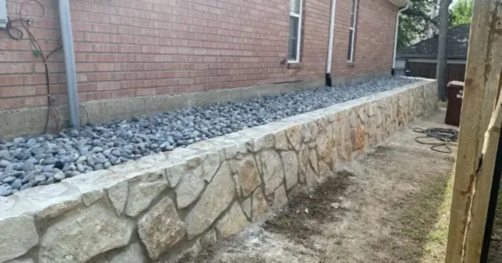 New Milsap stone retaining wall alongside a brick home with gravel drainage bed, replacing a failing wall in Denton, TX