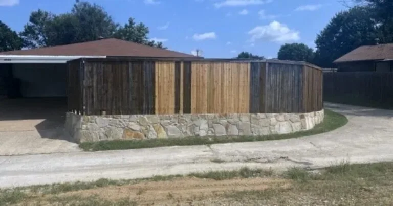 Curved Milsap stone retaining wall base supporting a wood privacy fence at a residential property in Garland, TX