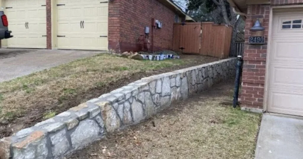 New Milsap stone retaining wall along front yard driveway border replacing failed wood crosstie wall at brick home in Highland Village, TX