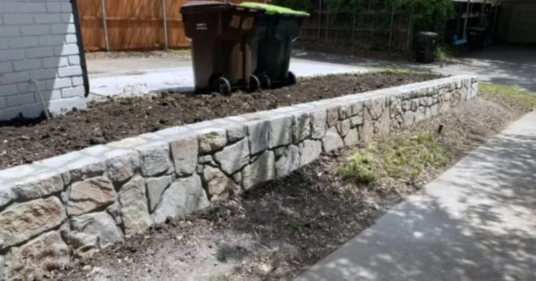 Newly built Milsap stone retaining wall along a residential driveway in Plano, TX, replacing an old cinderblock wall with fresh backfill soil