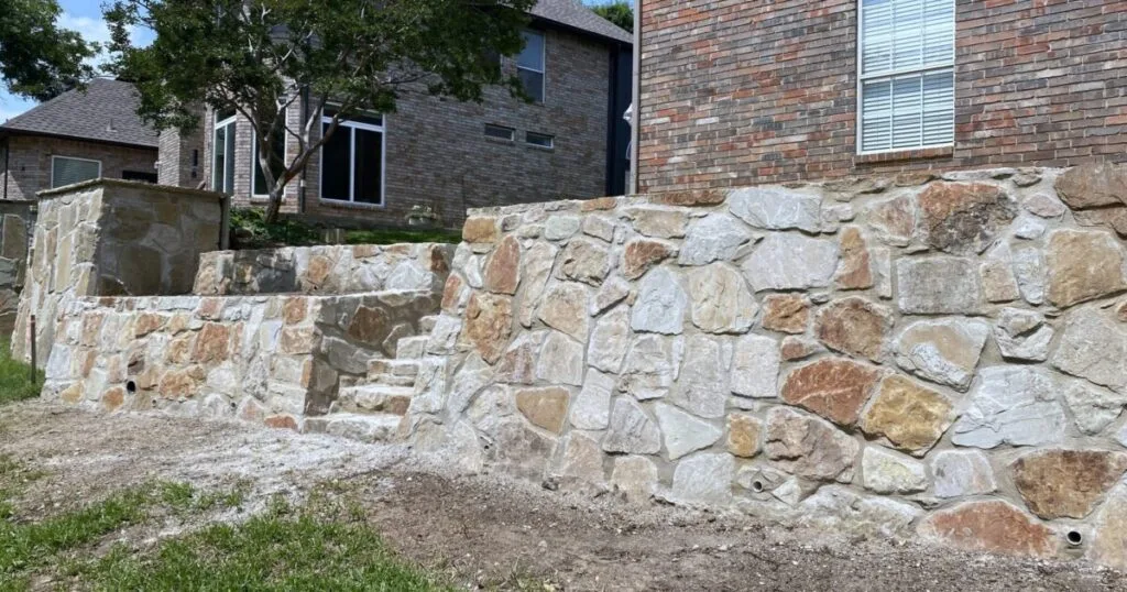 Tiered Milsap stone retaining wall with integrated steps replacing a failed cross-tie wall beside a brick home in Colleyville TX