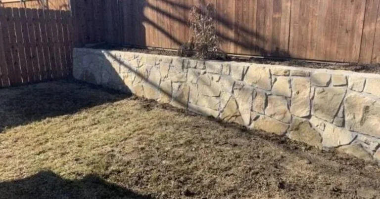 Newly built Milsap stone retaining wall replacing a failed crosstie wall in a Frisco TX backyard, raising a planting bed along a wood fence.
