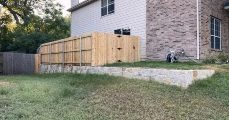 New Milsap stone retaining wall levels a sloped side yard beside a brick home in DFW, with a cedar privacy fence installed on top.