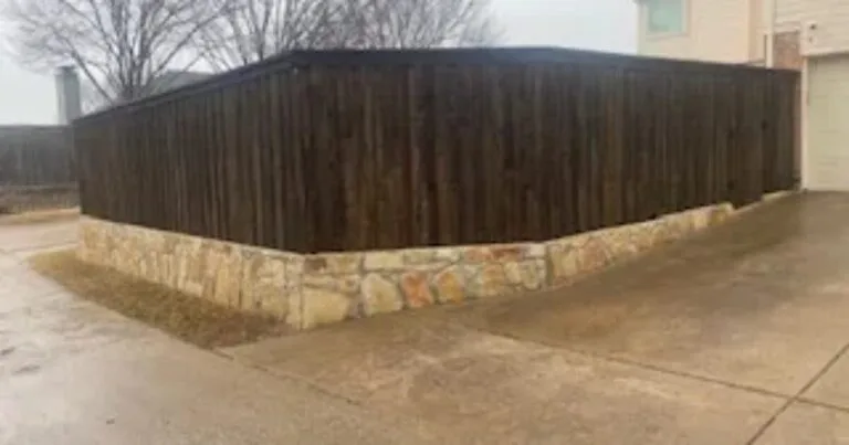 Low Milsap stone retaining wall base supporting a dark wood privacy fence along a residential concrete driveway in DFW