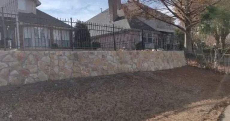Completed Milsap stone retaining wall with reinstalled wrought iron fence replacing old cross tie wall at a Flower Mound residential property
