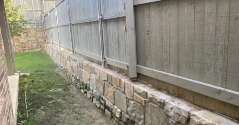 Low Milsap stone retaining wall running along a wood privacy fence in a narrow residential side yard, leveling the grade in the Dallas–Fort Worth area.
