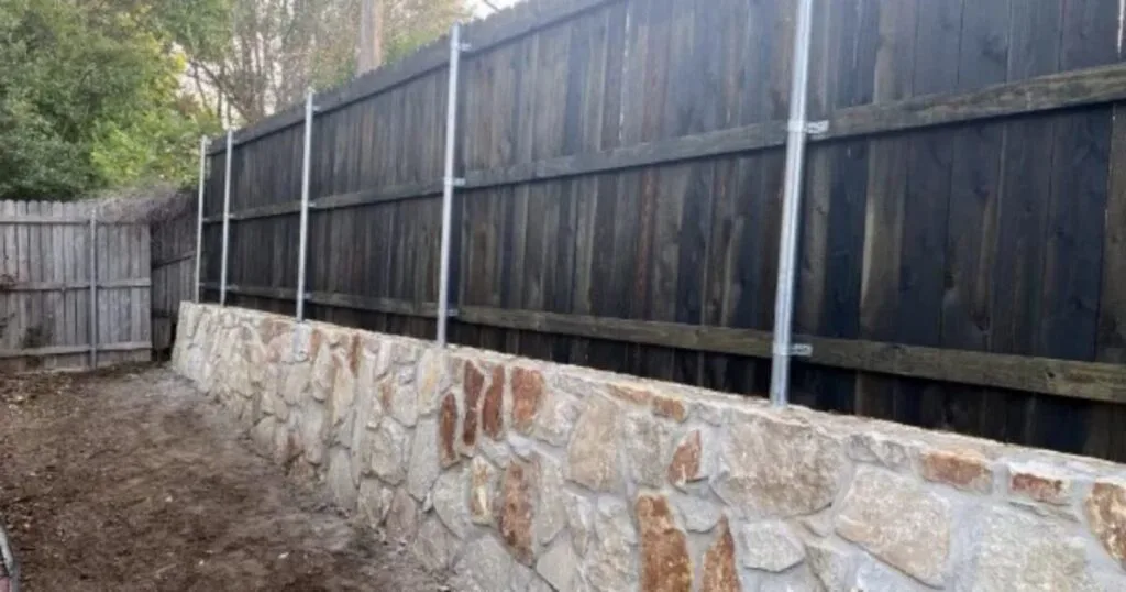 Milsap stone retaining wall replacing failed railroad cross-tie wall, topped with new dark cedar fence and galvanized steel posts, DFW backyard