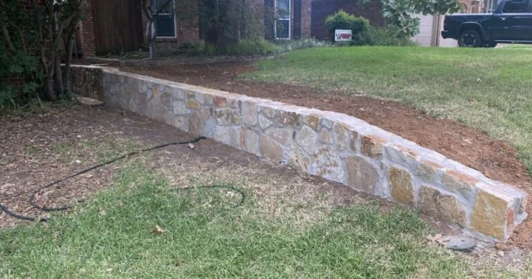 Newly built Milsap stone retaining wall replacing a wood wall along a residential front yard in DFW, with fresh backfill soil visible behind it
