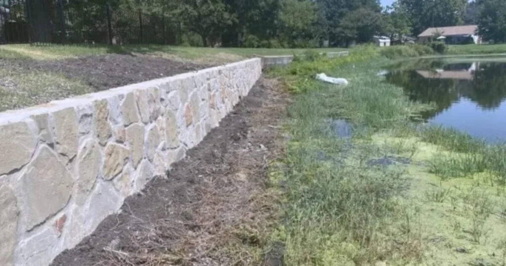 Newly built Milsap stone retaining wall replacing old cross ties along a pond waterfront in DFW, protecting yard from erosion