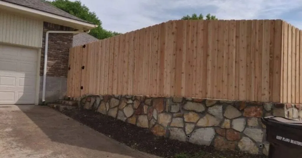 Natural stone retaining wall supporting a cedar privacy fence along a residential driveway in Plano, TX