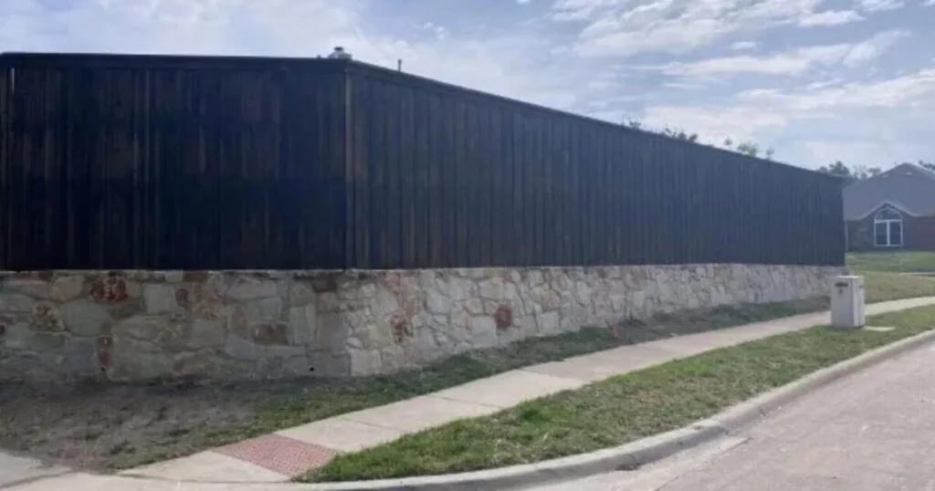 Long natural stone retaining wall base supporting a dark wood privacy fence along a residential street in DFW
