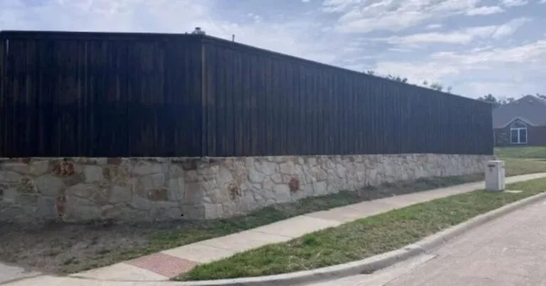 Long natural stone retaining wall base supporting a dark wood privacy fence along a residential street in DFW