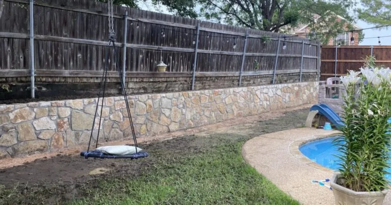 Newly built natural stone retaining wall along backyard fence line next to a residential pool in Euless, TX