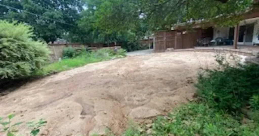 Backyard after partial pool removal in Dallas TX — compacted sandy fill and finish grading restore usable yard space next to covered patio