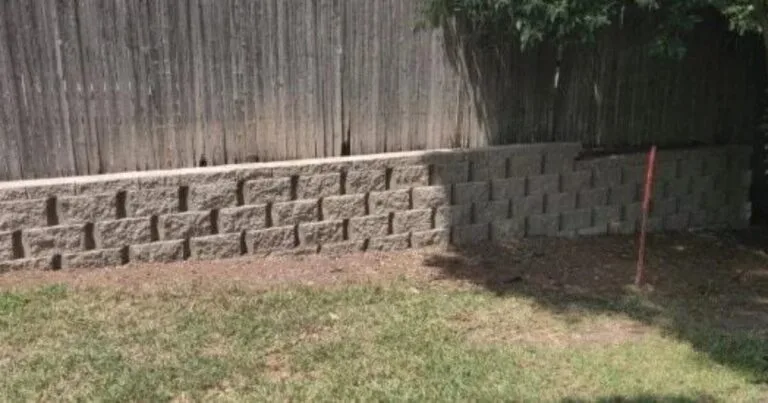 Concrete block retaining wall along a wood privacy fence in a DFW backyard, built with Pavestone Regal-line blocks for erosion control and soil retention in Coppell, TX.