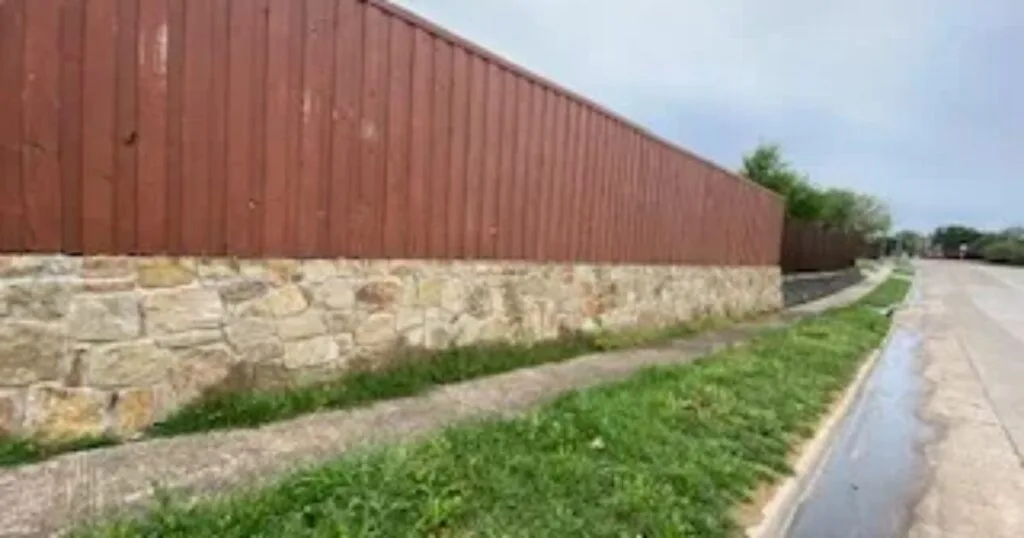 Existing stone base retaining wall topped with red wood fence along a Carrollton TX roadside, candidate for Milsap stone replacement by JCL Landscape Services